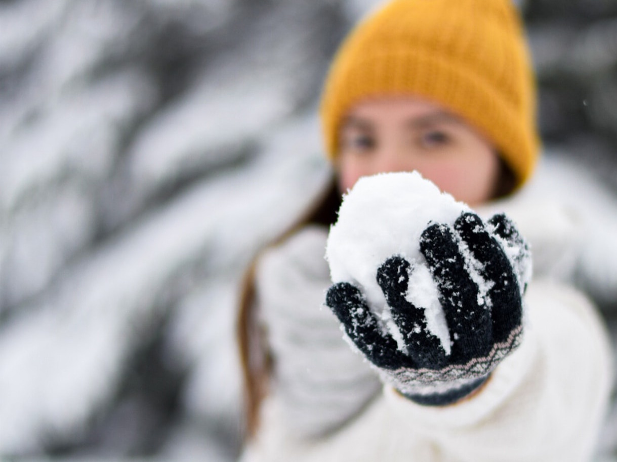 Femme avec un bonnet jaune qui tient une boule de neige